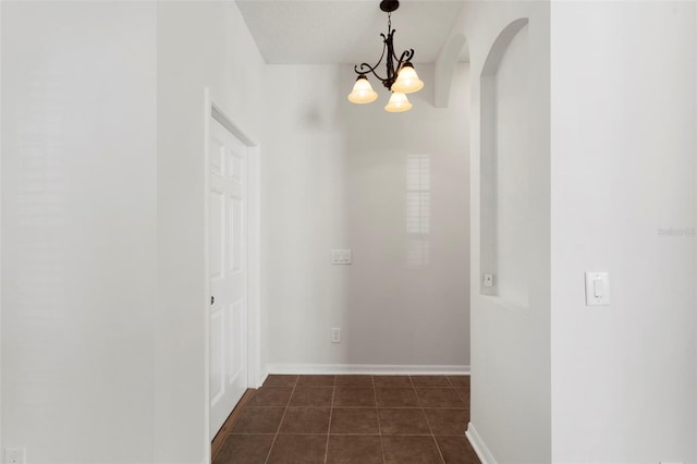 hall featuring arched walkways, dark tile patterned floors, an inviting chandelier, and baseboards