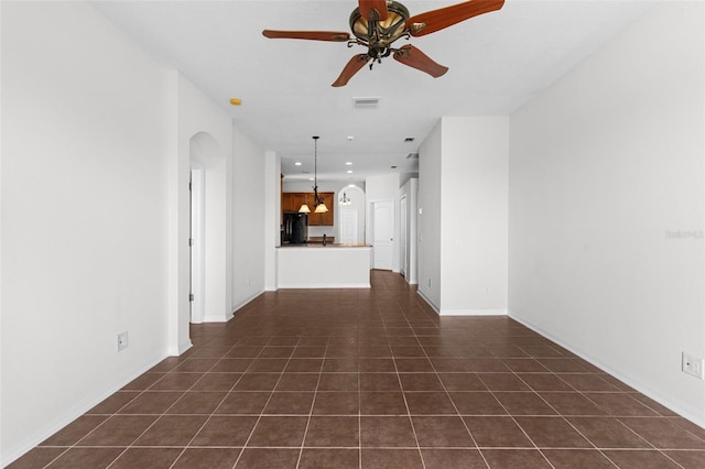 unfurnished living room with a ceiling fan, arched walkways, visible vents, and dark tile patterned floors