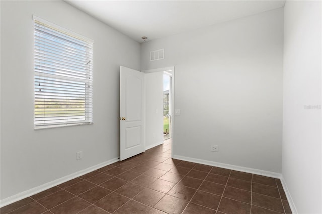 empty room featuring dark tile patterned flooring, visible vents, and baseboards