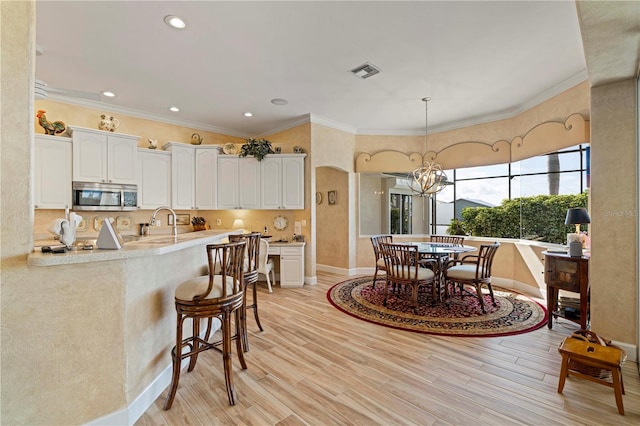 kitchen featuring crown molding, white cabinetry, decorative light fixtures, and light wood-type flooring