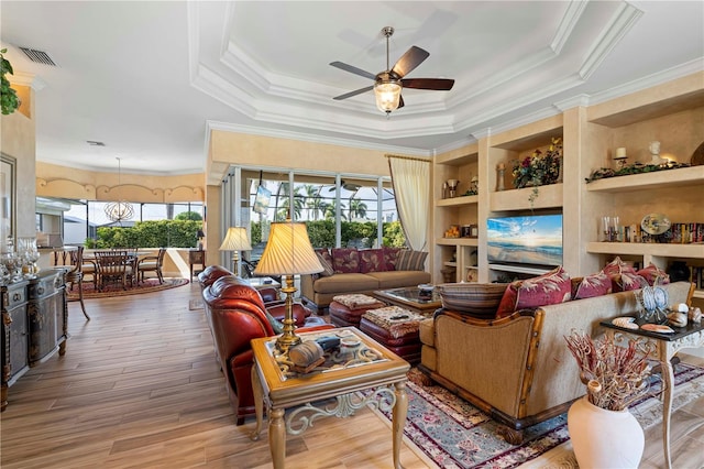 living room with ornamental molding, a tray ceiling, light wood-type flooring, and ceiling fan