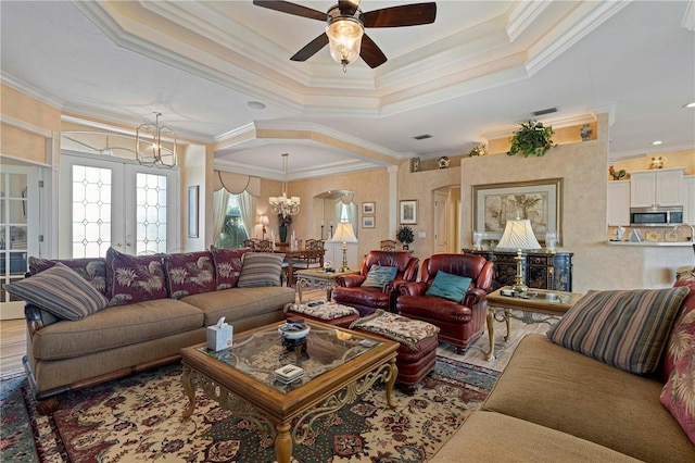 living room featuring hardwood / wood-style flooring, a tray ceiling, ornamental molding, ceiling fan with notable chandelier, and french doors