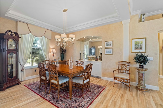 dining space featuring light hardwood / wood-style flooring, ornamental molding, a tray ceiling, and a notable chandelier