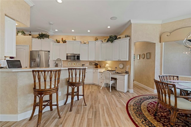 kitchen with appliances with stainless steel finishes, light hardwood / wood-style flooring, white cabinets, and ornamental molding