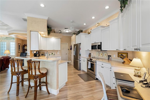 kitchen with kitchen peninsula, white cabinets, light hardwood / wood-style flooring, ornamental molding, and stainless steel appliances