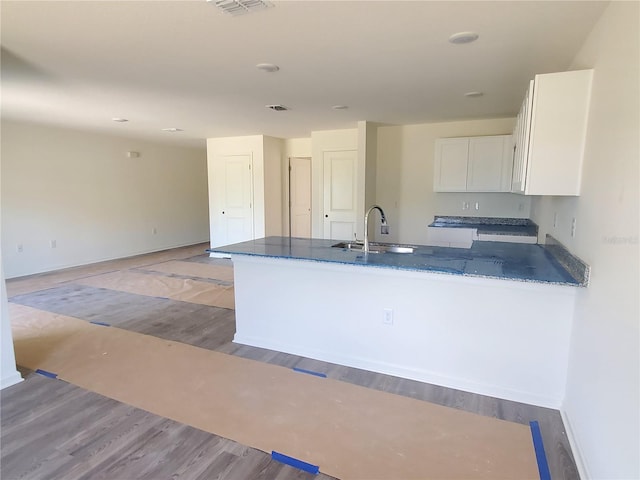 kitchen featuring kitchen peninsula, dark stone counters, sink, light hardwood / wood-style flooring, and white cabinetry