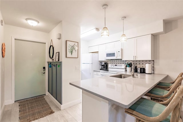 kitchen with white appliances, kitchen peninsula, hanging light fixtures, white cabinetry, and a breakfast bar area