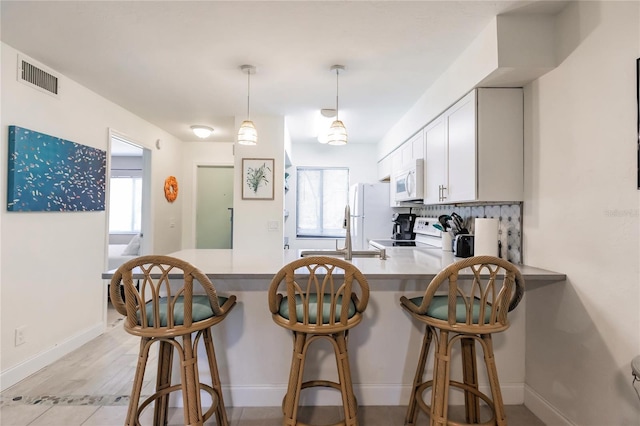 kitchen featuring white cabinets, plenty of natural light, kitchen peninsula, and white appliances