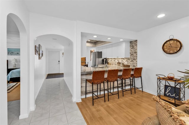 kitchen with stainless steel fridge, kitchen peninsula, light hardwood / wood-style flooring, white cabinetry, and a breakfast bar area