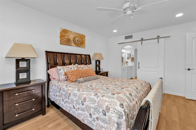 bedroom featuring a barn door, connected bathroom, light hardwood / wood-style flooring, and ceiling fan