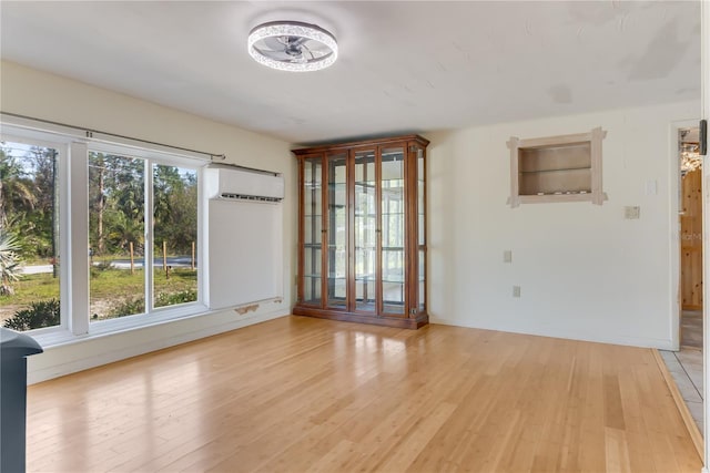 empty room with a wall mounted AC, light wood-type flooring, and a wealth of natural light