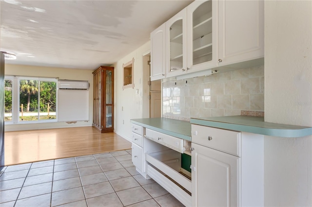 kitchen with white cabinetry, light tile patterned floors, decorative backsplash, and a wall unit AC