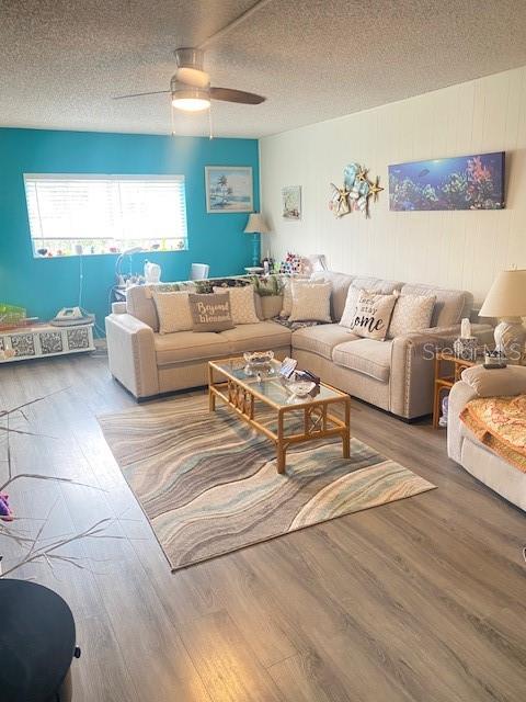 living room featuring hardwood / wood-style flooring, ceiling fan, and a textured ceiling