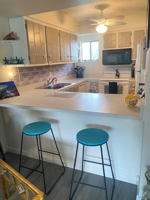 kitchen with a kitchen breakfast bar, kitchen peninsula, white appliances, and tasteful backsplash