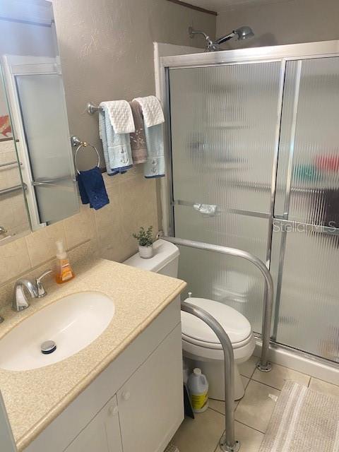 bathroom with tile patterned flooring, toilet, decorative backsplash, a shower with door, and vanity