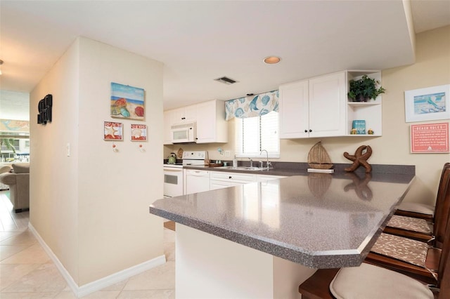 kitchen with white cabinets, kitchen peninsula, white appliances, and a kitchen bar