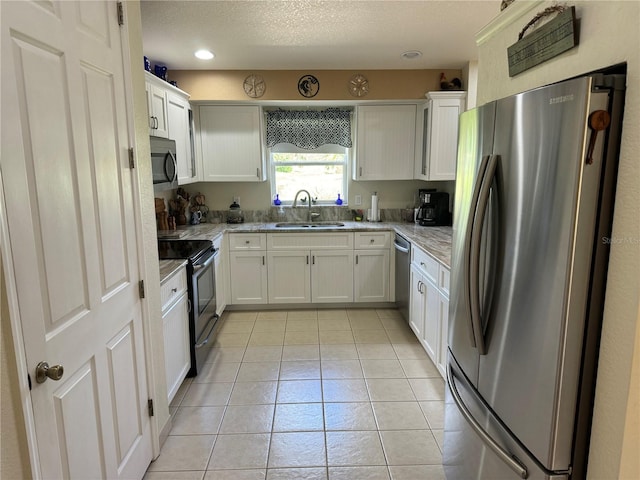 kitchen with white cabinets, light tile patterned floors, sink, appliances with stainless steel finishes, and light stone countertops