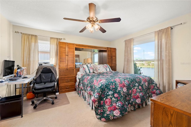 bedroom with a water view, ceiling fan, multiple windows, and light colored carpet