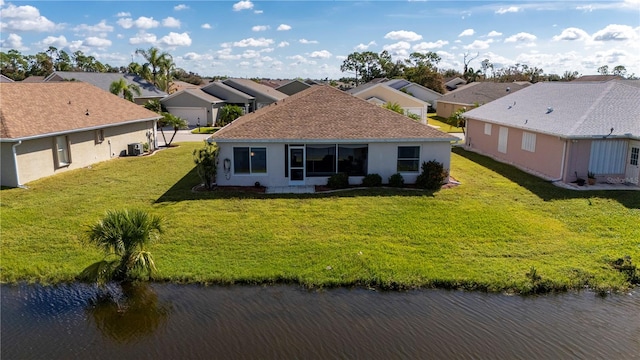 rear view of house featuring a water view, a sunroom, and a lawn