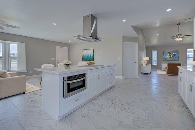 kitchen with open floor plan, ceiling fan, stainless steel oven, wall chimney exhaust hood, and white cabinetry