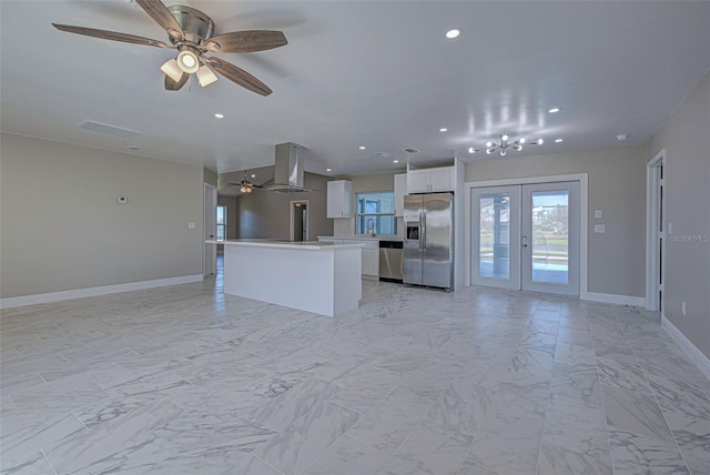 kitchen with ceiling fan with notable chandelier, a center island, appliances with stainless steel finishes, island range hood, and white cabinetry