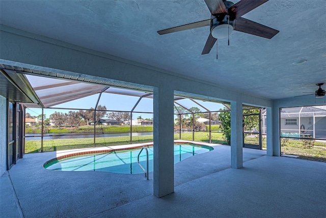 pool featuring glass enclosure, a water view, a ceiling fan, and a patio area