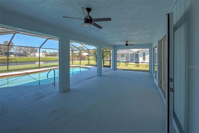 pool with glass enclosure, a water view, ceiling fan, and a patio area