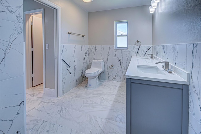 full bath featuring double vanity, toilet, tile walls, a wainscoted wall, and a sink