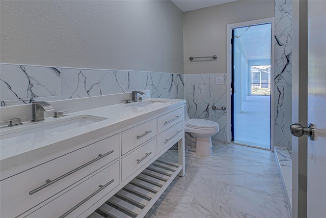 full bath with a sink, marble finish floor, toilet, and tile walls