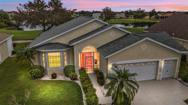 view of front of home with a garage, a lawn, and a water view