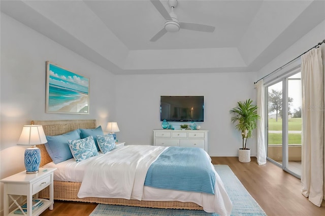 bedroom with ceiling fan, access to outside, a tray ceiling, and wood-type flooring