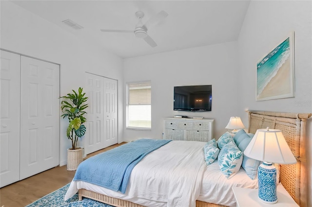 bedroom featuring ceiling fan, two closets, and light hardwood / wood-style flooring