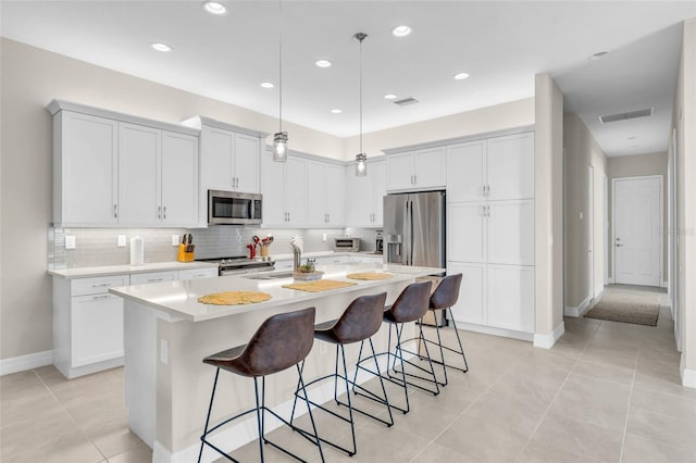 kitchen featuring hanging light fixtures, a center island with sink, light tile patterned floors, appliances with stainless steel finishes, and white cabinetry