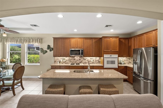 kitchen with appliances with stainless steel finishes, light tile patterned flooring, sink, and an island with sink