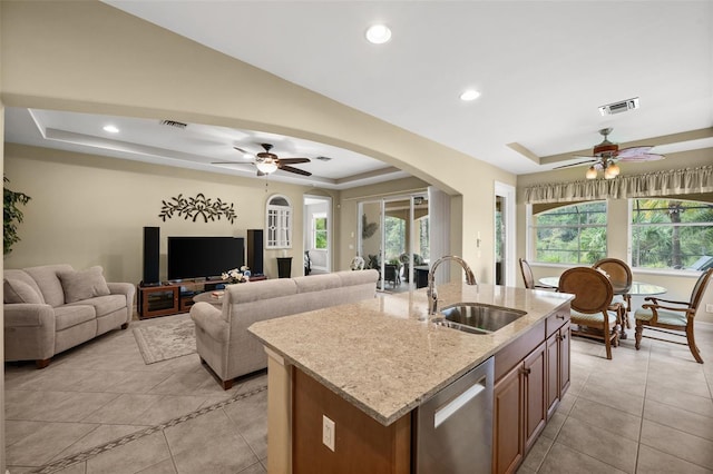 kitchen with sink, an island with sink, dishwasher, and a tray ceiling