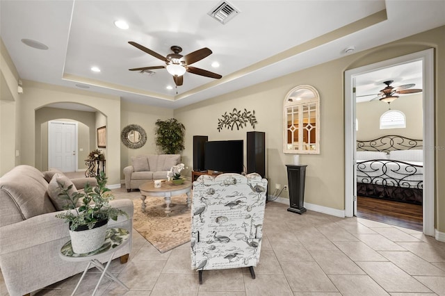 living room featuring light tile patterned flooring, ceiling fan, and a raised ceiling