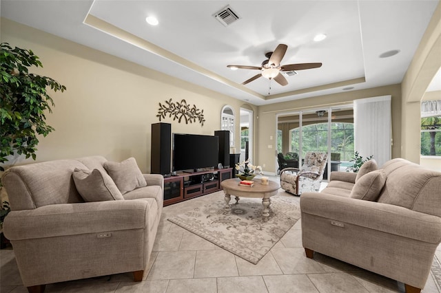 tiled living room with ceiling fan and a raised ceiling