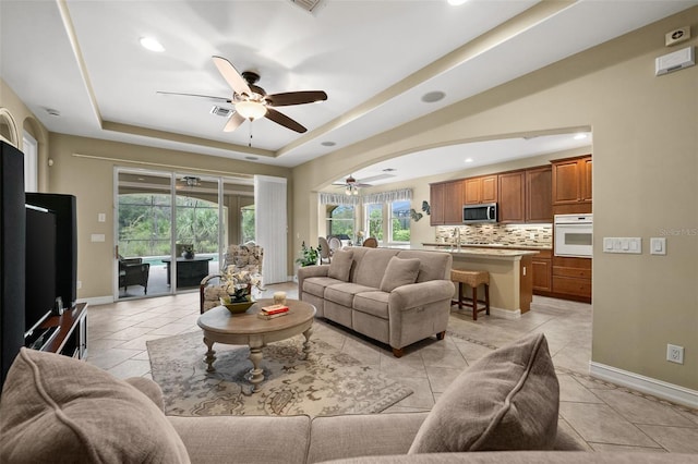 living room with light tile patterned flooring, a tray ceiling, and ceiling fan