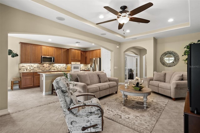 tiled living room with a tray ceiling and ceiling fan