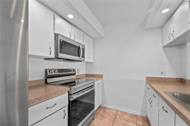 kitchen with sink, light tile patterned flooring, stainless steel appliances, and white cabinetry