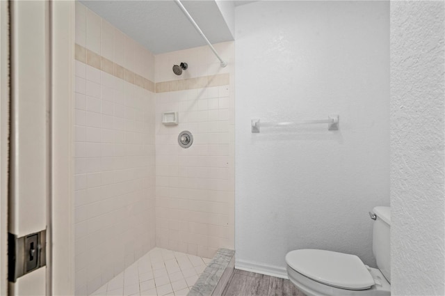 bathroom featuring toilet, wood-type flooring, and tiled shower