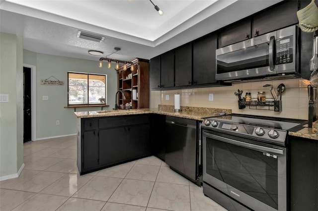 kitchen with sink, stainless steel appliances, light stone counters, kitchen peninsula, and decorative backsplash