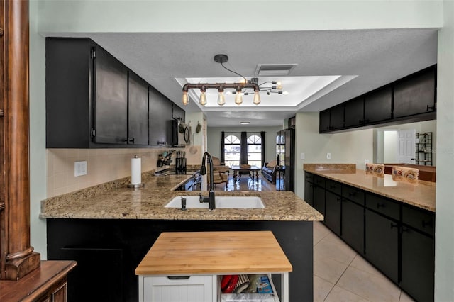 kitchen featuring sink, light stone counters, kitchen peninsula, decorative light fixtures, and light tile patterned floors