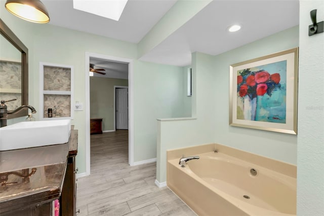 bathroom featuring vanity, a tub to relax in, a skylight, and ceiling fan