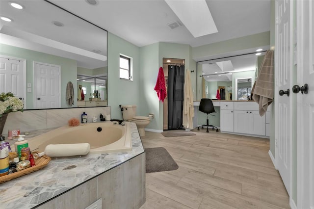 bathroom with vanity, a skylight, hardwood / wood-style flooring, toilet, and tiled tub