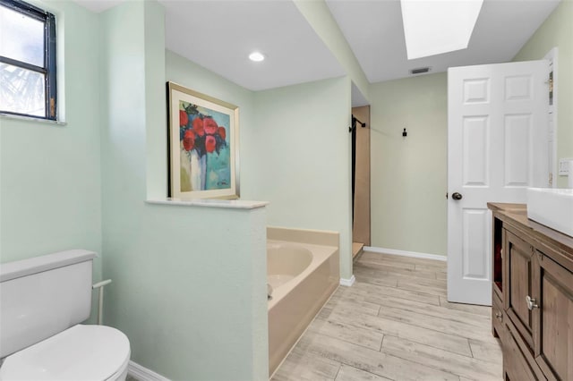 bathroom with a skylight, vanity, hardwood / wood-style flooring, toilet, and a bathing tub