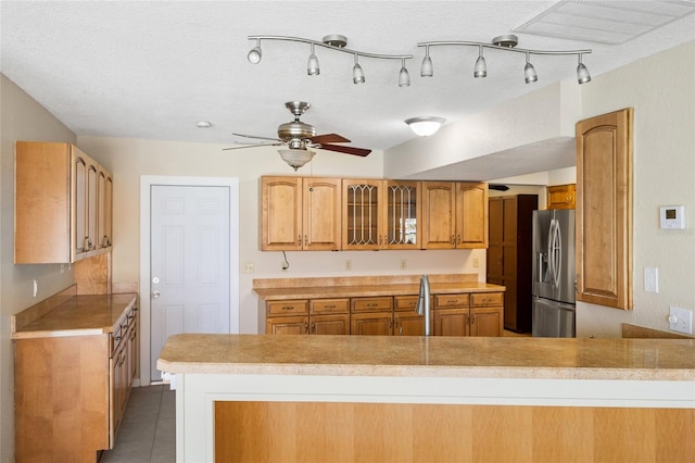 kitchen featuring sink, a textured ceiling, kitchen peninsula, stainless steel fridge, and tile patterned floors