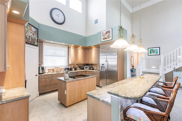 kitchen featuring stainless steel built in fridge, a kitchen island, hanging light fixtures, light stone counters, and a towering ceiling