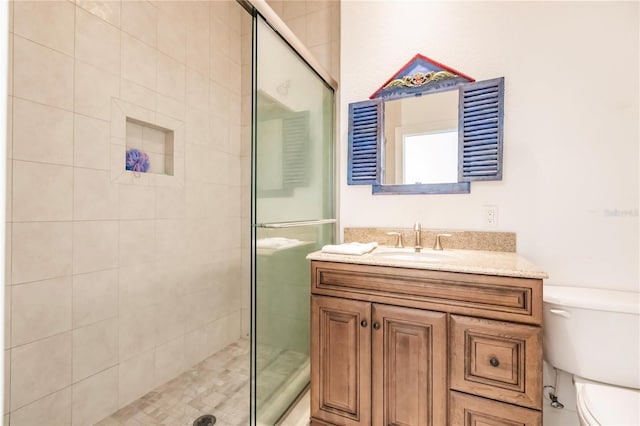 bathroom featuring toilet, a shower with shower door, and vanity