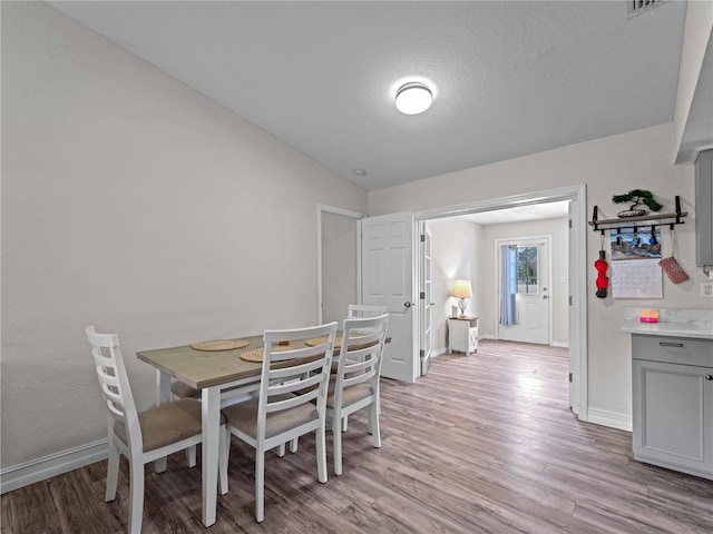 dining area with light hardwood / wood-style floors, vaulted ceiling, and a textured ceiling